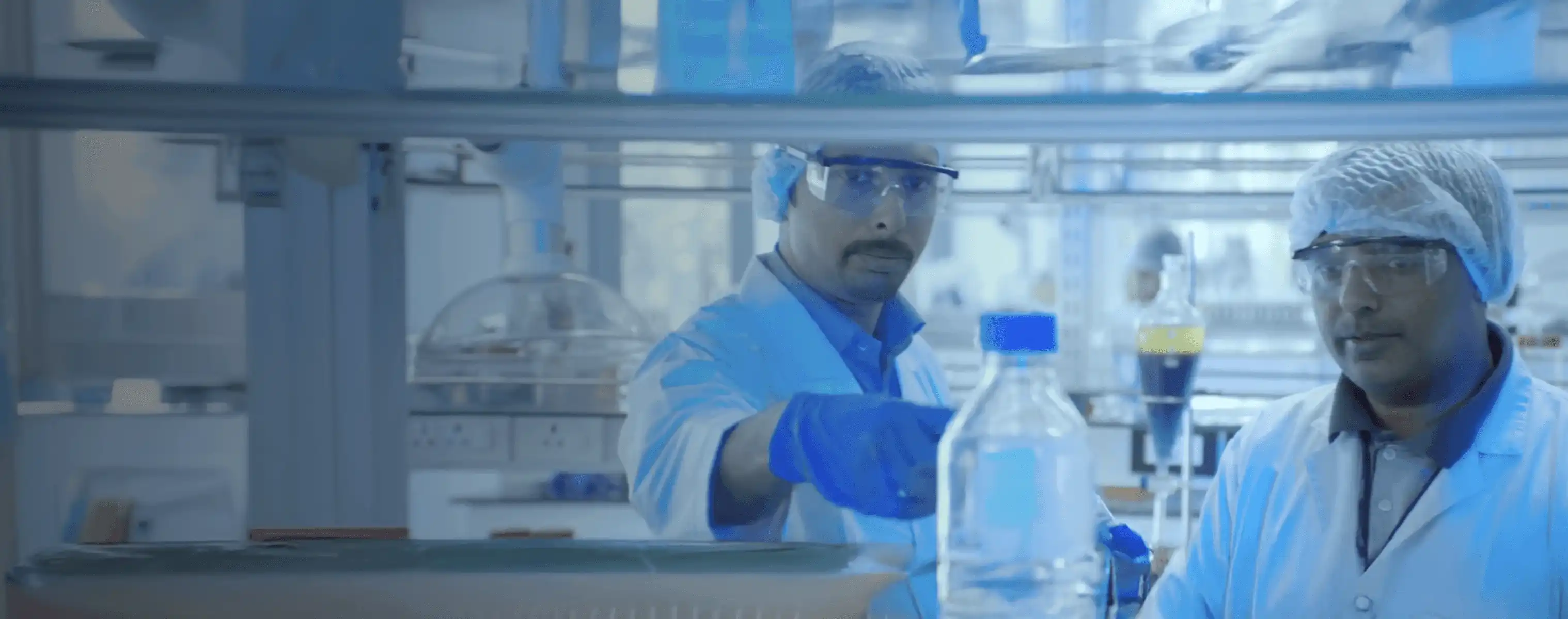 Two researchers wearing lab coats and safety gear analyzing chemical samples in a high-tech Synthite laboratory.